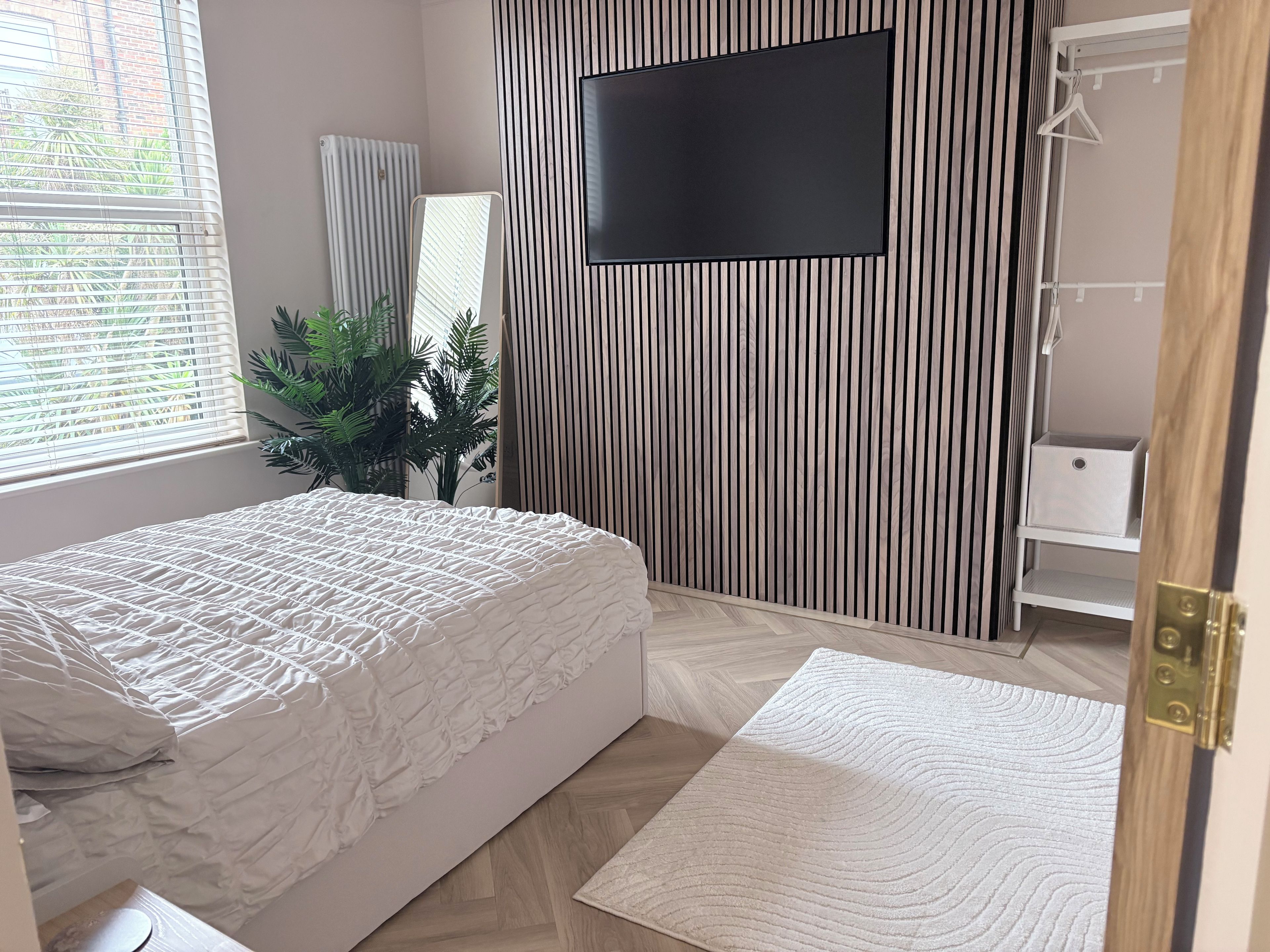 Une chambre à coucher avec un lit, un téléviseur fixé au mur, un radiateur et une plante.