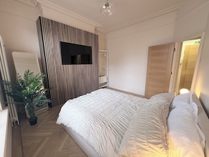 A bedroom with a bed, a television mounted on a wall, a wardrobe, and a potted plant.