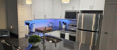 Cozinha moderna com armários brancos, eletrodomésticos de aço inoxidável e bancada de granito.