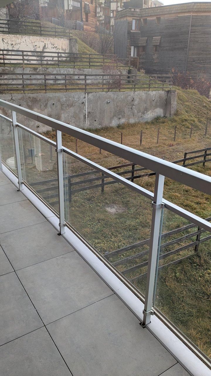 Un balcón de concreto con barandilla metálica que da a un área verde con un edificio al fondo.