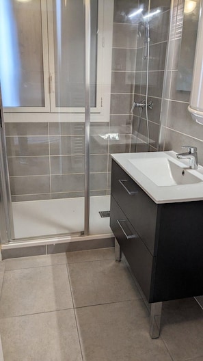 Ein Badezimmer mit Duschkabine aus Glas, einem weißen Waschbecken und einem dunklen Waschtisch.