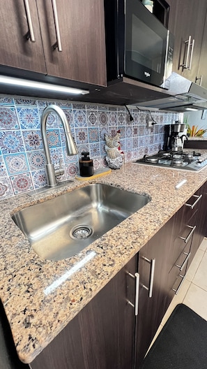 Een keuken met een roestvrijstalen spoelbak, donkerhouten kasten, een magnetron en een betegelde spatwand.