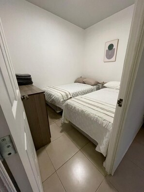Ett litet, rent rum med två sängar, ett träskåp och en tavla som hänger på väggen.