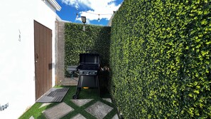 Un pati amb una barbacoa, una paret blanca i una tanca.