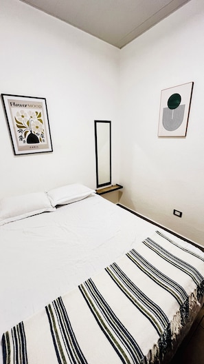 Een slaapkamer met een bed, nachtkastje, spiegel en twee decoratieve wandobjecten.