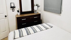 Ein Schlafzimmer mit Bett, Kommode, Spiegel, Fenster und Tür.