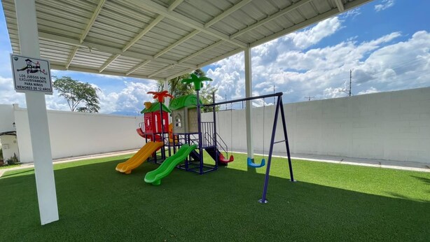 Ein Spielplatz mit Rutsche und Schaukeln unter einem Schutzdach.