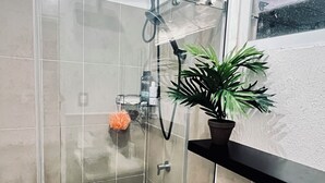Ein modernes Badezimmer mit Duschkabine aus Glas, Toilette und einer Topfpflanze.