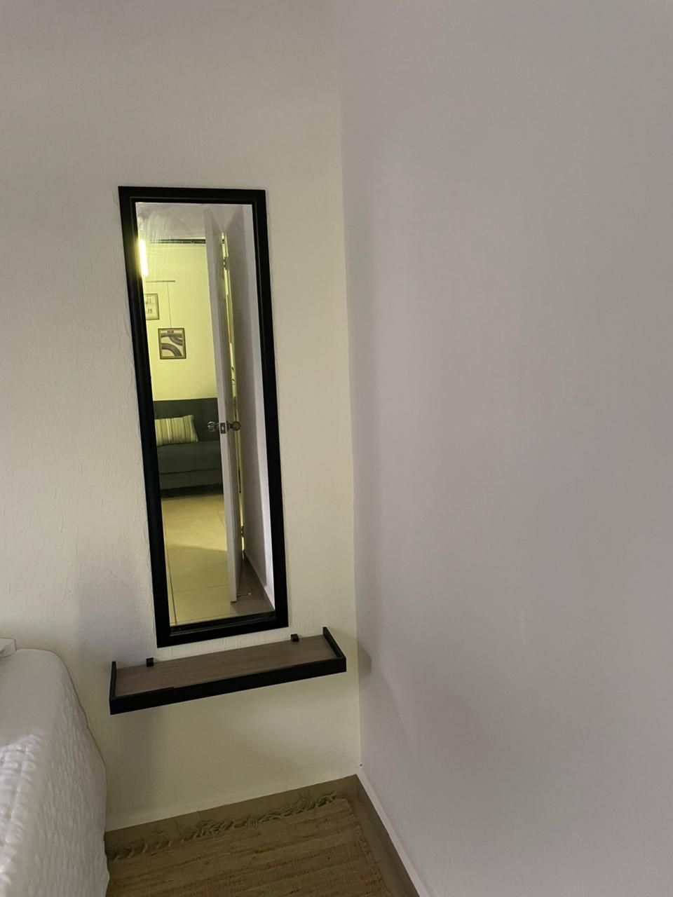 Ein Zimmer mit einem Bett, einem Spiegel und einer Tür zu einem anderen Raum.