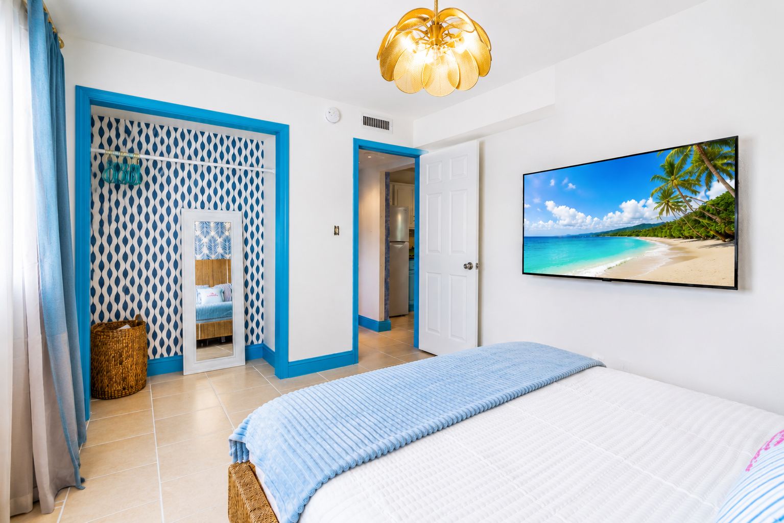 Een slaapkamer met een bed, een aan de muur bevestigde televisie waarop een strand te zien is, en een deur naar een badkamer.