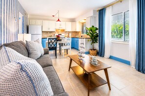 A modern living room with a sofa, a wooden coffee table, and a kitchen in the background with blue cabinets and a red pendant light. - Coastal Haven | Pet-Friendly | Near the Beach | Treasure Island (Treasure Island)