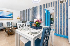 A dining area with a table set for two, a blue chair, and a wall with vertical stripes. - Coastal Haven | Pet-Friendly | Near the Beach | Treasure Island (Treasure Island)