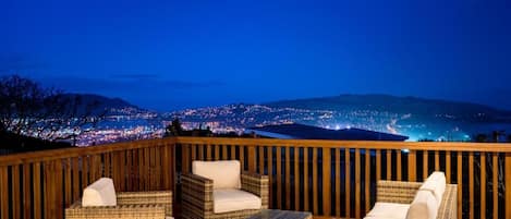 A balcony with wicker furniture and a view of a cityscape at night.