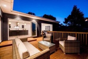 Terraza exterior con mobiliario de mimbre, zona de bar y puerta corredera de vidrio que da a una cocina.