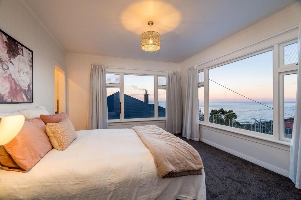 A bedroom with a large bed, a view of the sea, and a cityscape through the windows.