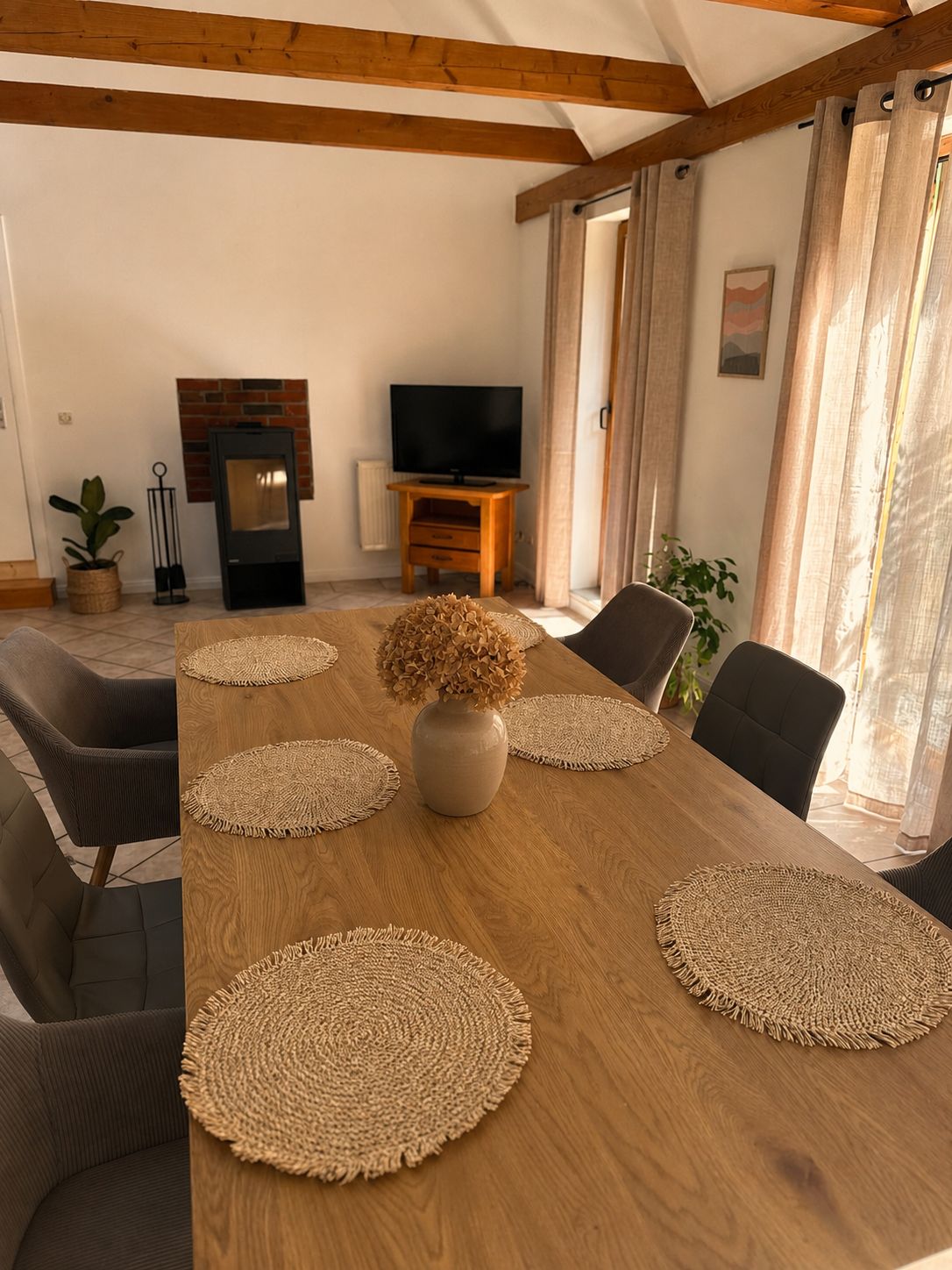 Ein Essbereich mit einem Holztisch, gewebten Untersetzern und einer Vase mit getrockneten Blumen.