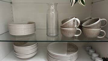 A glass shelf with stacked plates, a clear glass pitcher, and ceramic mugs.