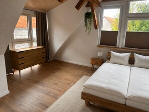 A bedroom with a wooden bed, a dresser, a nightstand, and a hanging plant.