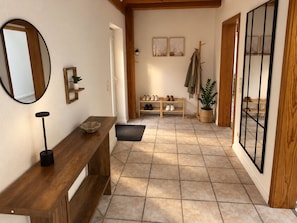 Un pasillo con un banco de madera, un espejo, un zapatero y una planta en maceta.
