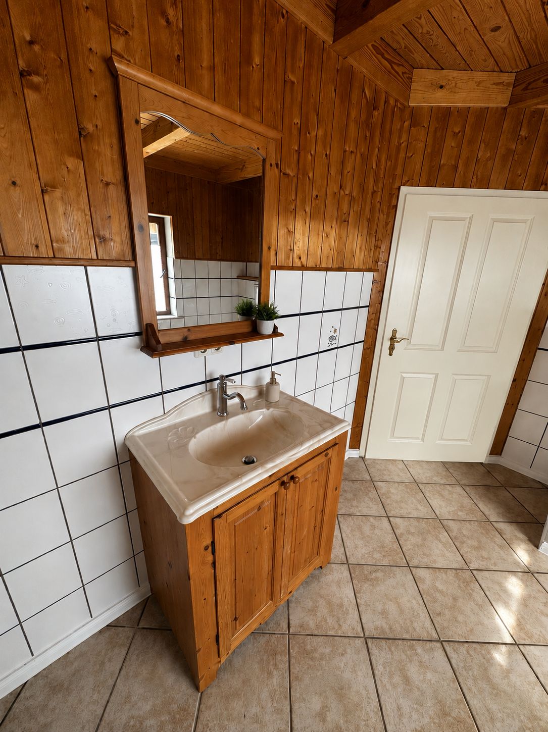 Une salle de bain en bois avec un lavabo, un miroir et des murs recouverts de carreaux blancs.