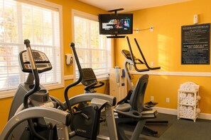 Une salle de sport équipée d’appareils de cardio, d’un téléviseur et d’un panneau affichant les règles de sécurité.
