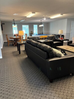 A living room with a pool table, leather sofas, and a dining area with chairs and a lamp. - Beautiful 1-bedroom condo in beach town Wells with an indoor pool (Wells)