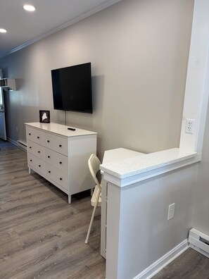 Ein Zimmer mit einem weißen Schminktisch, einem an der Wand befestigten Fernseher und einem kleinen weißen Stuhl.
