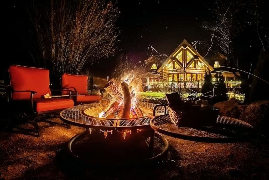 A fire pit with seating, a large house in the background, and a well-lit outdoor area.