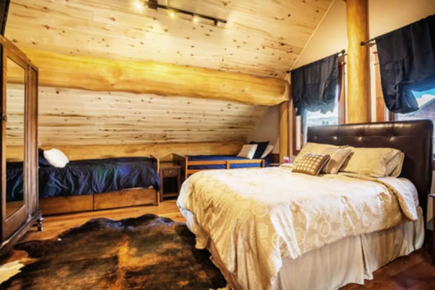 Un dormitorio de cabaña de madera con una cama grande, una cama más pequeña, una mesita de noche y un espejo.