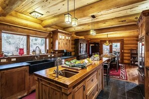 Eine Holzblockhausküche mit Holzausstattung, einer zentralen Kochinsel und Pendelleuchten.