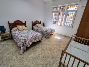A room with two beds, a crib, a window, and a nightstand.