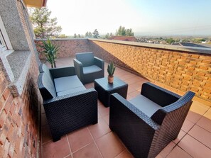 A rooftop terrace with wicker furniture, a small table, and a potted plant.