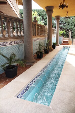A pool area with tiled flooring, columns, and potted plants.