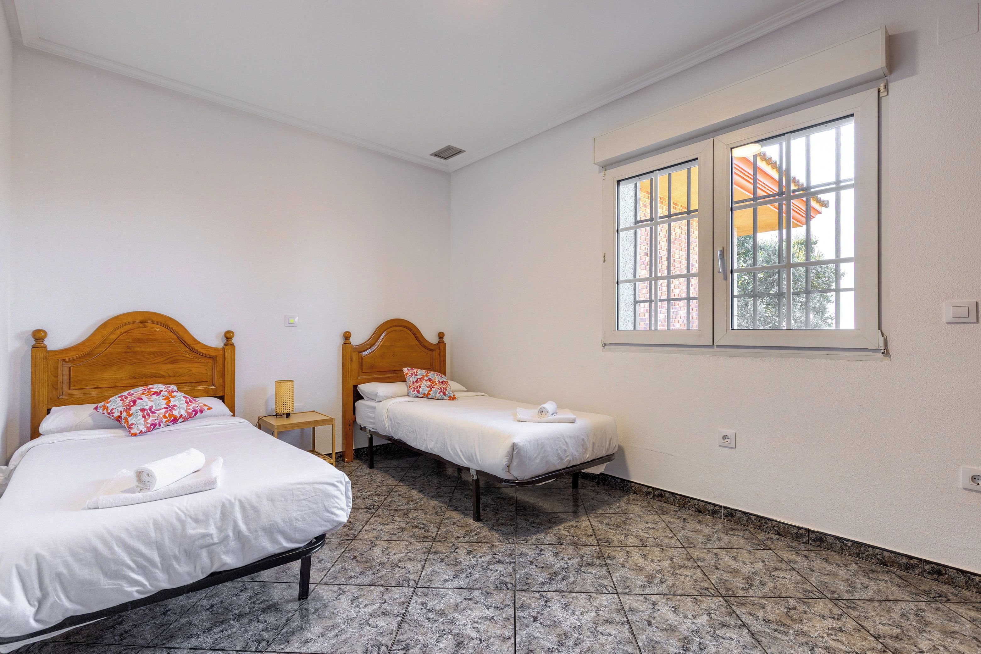 Una habitación de hotel con dos camas individuales, ventana con vistas y suelo de baldosas.