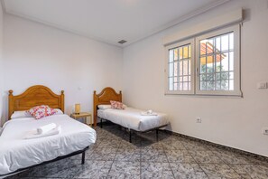 A hotel room with two single beds, a window with a view, and a tiled floor.
