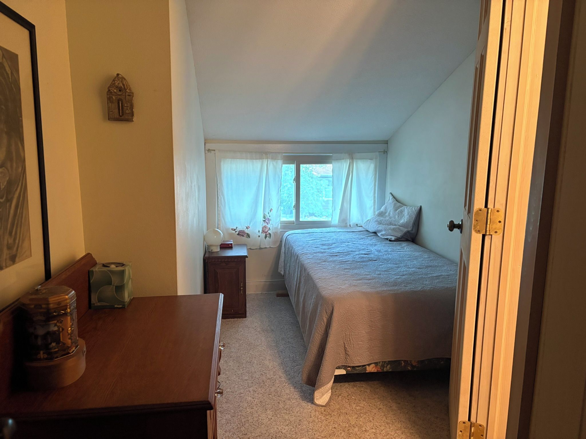 Une chambre à coucher avec un lit, une table de chevet, une commode et une fenêtre avec des rideaux.
