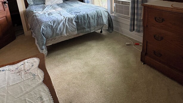 Une chambre à coucher avec un lit, une commode, une fenêtre avec des rideaux et un ventilateur de plafond.