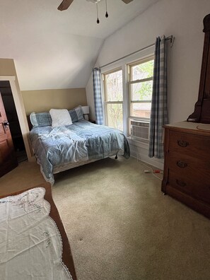 A bedroom with a bed, a dresser, a window with curtains, and a ceiling fan.