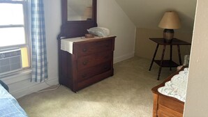 Une chambre à coucher avec une commode, un miroir, une lampe et une fenêtre avec des rideaux.