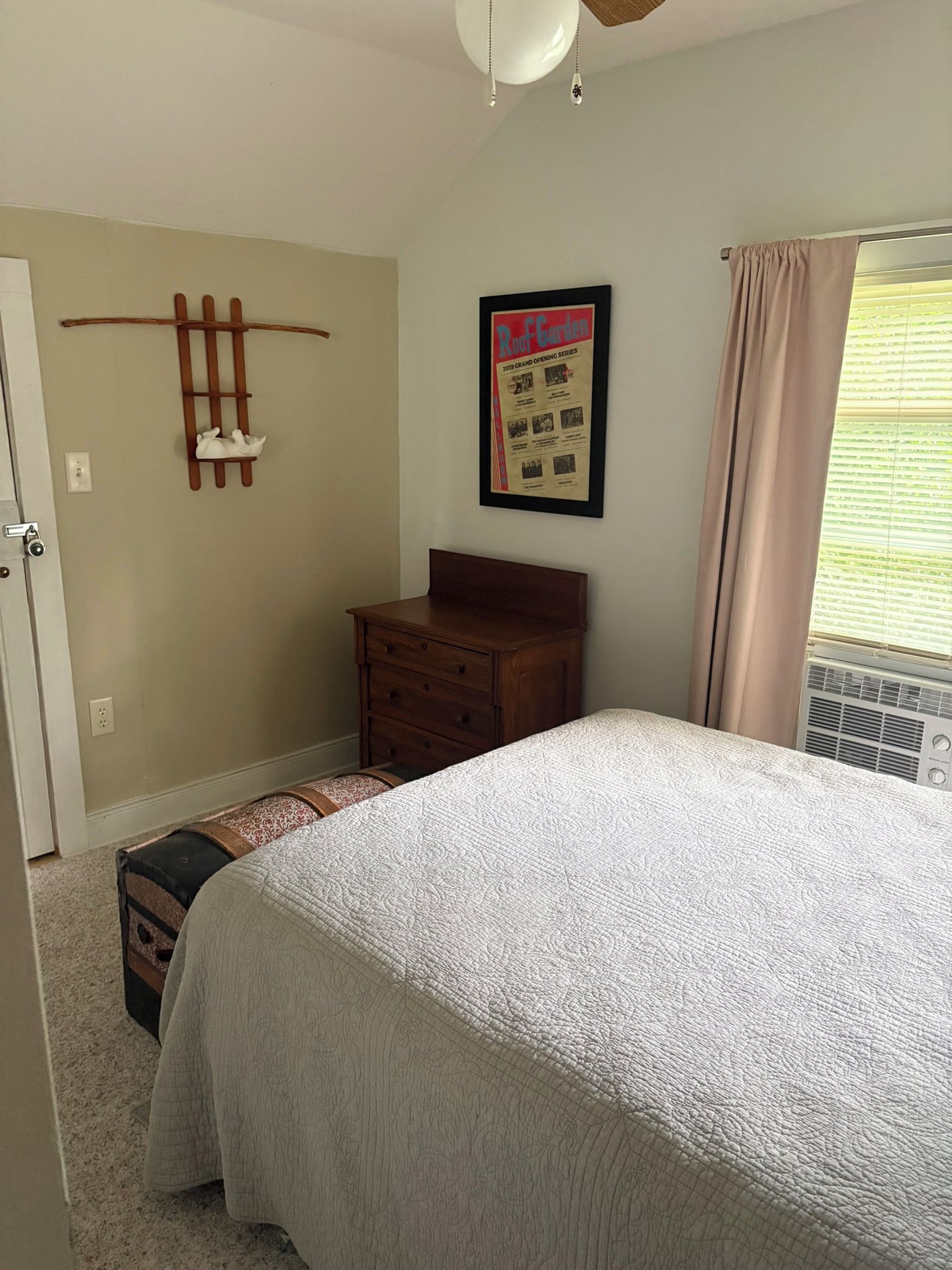 Une chambre à coucher comprenant un lit, une commode, une étagère fixée au mur et une affiche encadrée.