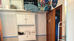 Une salle de bain avec un lavabo, un panier à linge, une étagère avec des serviettes pliées et une porte donnant sur une autre pièce.