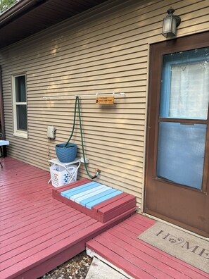 A house with a red deck, a blue and white pet washing station, and a brown door with a doormat.
