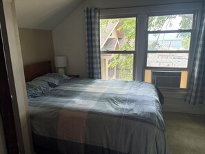 Ein Schlafzimmer mit einem Bett, einem Nachttisch, einer Lampe und einem Fenster mit Vorhängen.