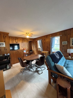 Ein gemütlicher Raum mit Holzvertäfelung, einem Esstisch mit Stühlen, einem Sofa und einem Deckenventilator.