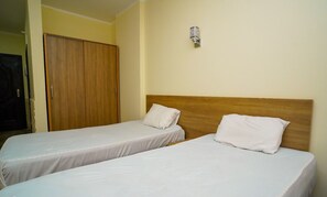 Une chambre d’hôtel avec deux lits simples, une tête de lit en bois, une armoire et un luminaire fixé au mur.