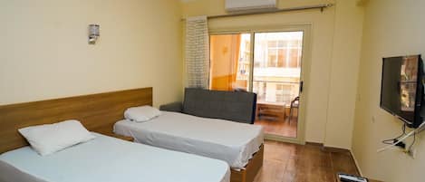Hotellihuone, jossa on kaksi sänkyä, televisio ja parveke, jossa on pöytä ja tuolit.