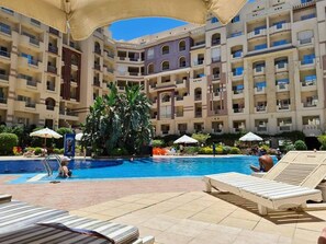Un espace piscine d’hôtel doté de plusieurs niveaux de balcons, de chaises longues et de parasols.