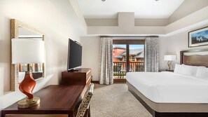 Habitación de hotel con cama, escritorio con televisor, silla, lámpara y vista al exterior.