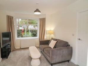 A living room with a television, sofa, bench, lamp, and window with curtains. - No.40 Rufford Road (Nottingham)