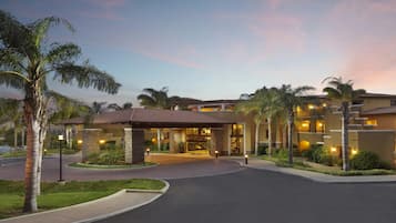 Un hotel con entrada cubierta, palmeras y una entrada de acceso curva.